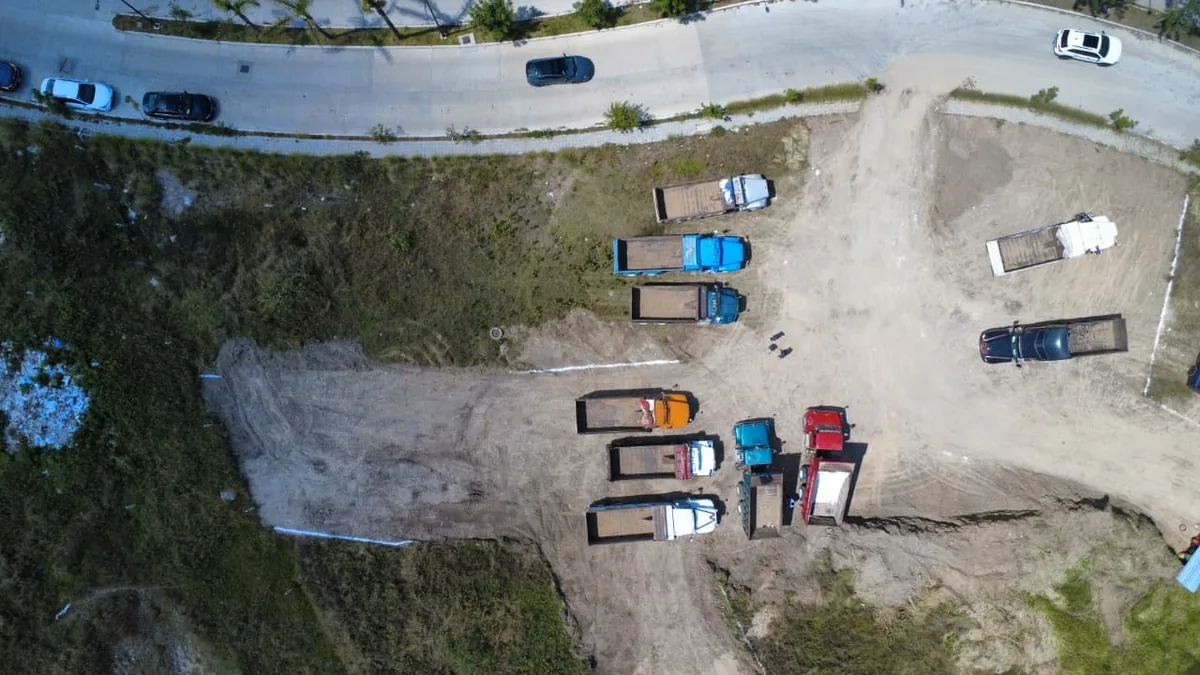 Vista cenital de camiones de volteo formados en terreno despalmado junto al bulevar