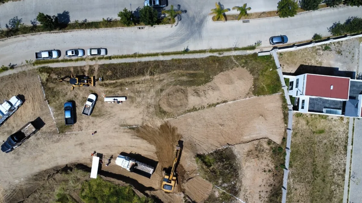 Excavadora y retroexcavadora cortando y nivelando el terreno, con camionetas de apoyo